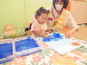 保育園で先生と絵の具遊びをする子供の様子の写真