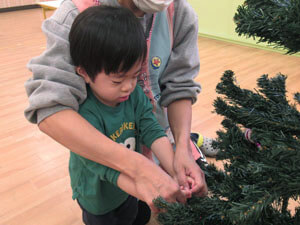 保育園で園児がもみの木にクリスマスの飾り付けをしている様子